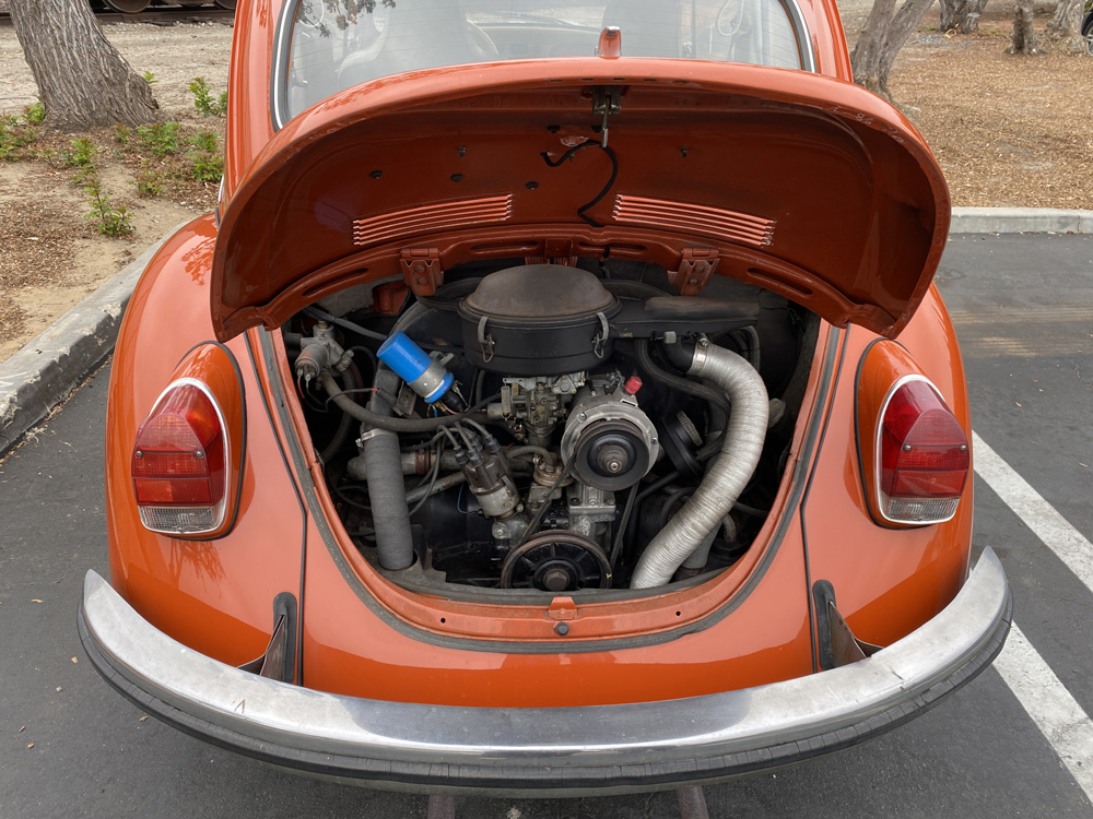 Open rear engine compartment of an orange Volkswagen Beetle.