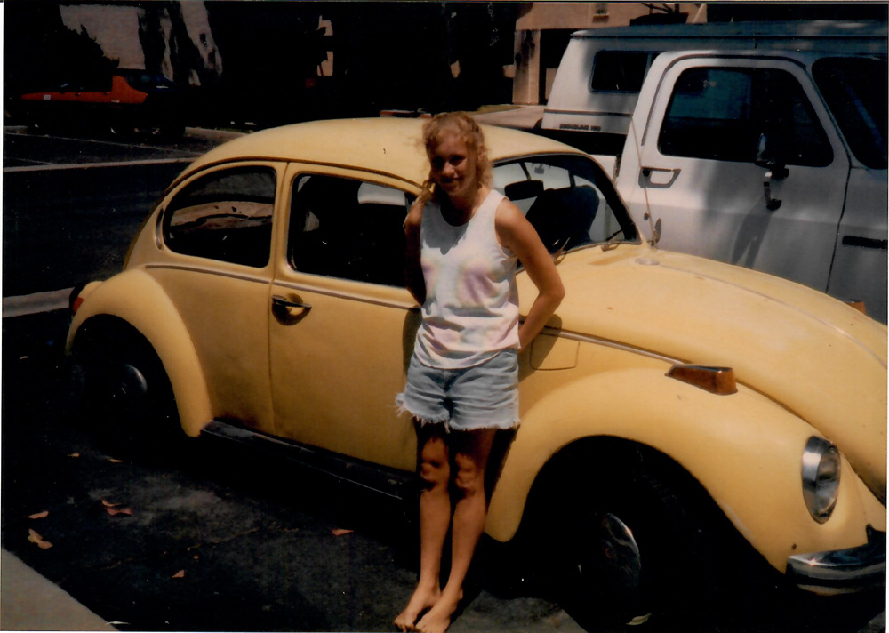 Erika standing beside a yellow Volkswagen Beetle on a residential street.