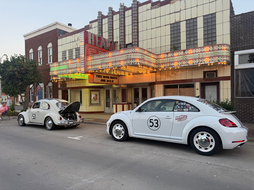 An old and a new Beetle parked by a movie theatre